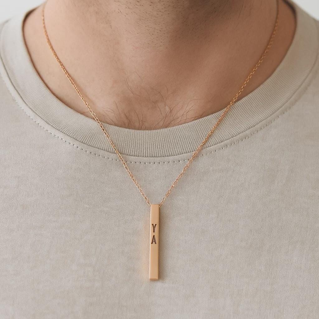 Gold necklace with a vertical bar pendant on a plain background