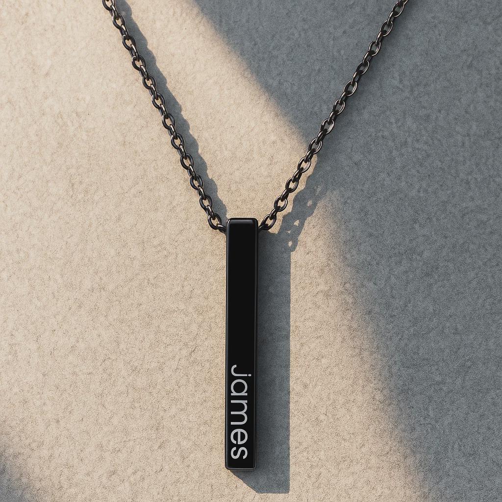 Black necklace with a bar pendant engraved with 'James' on a textured surface